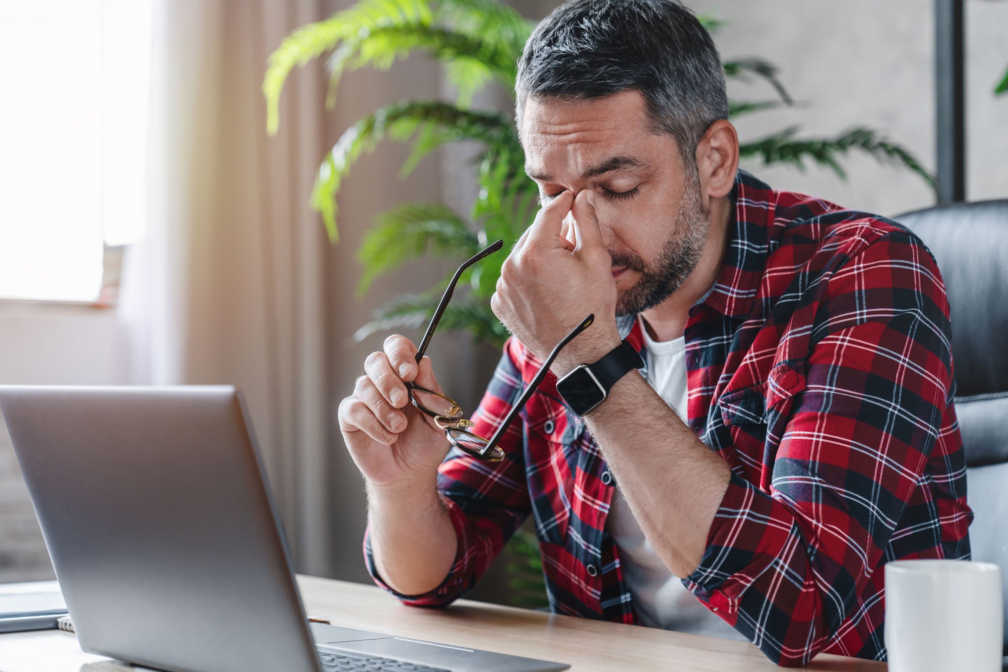 Man sitting at laptop holding forehead and looking tired