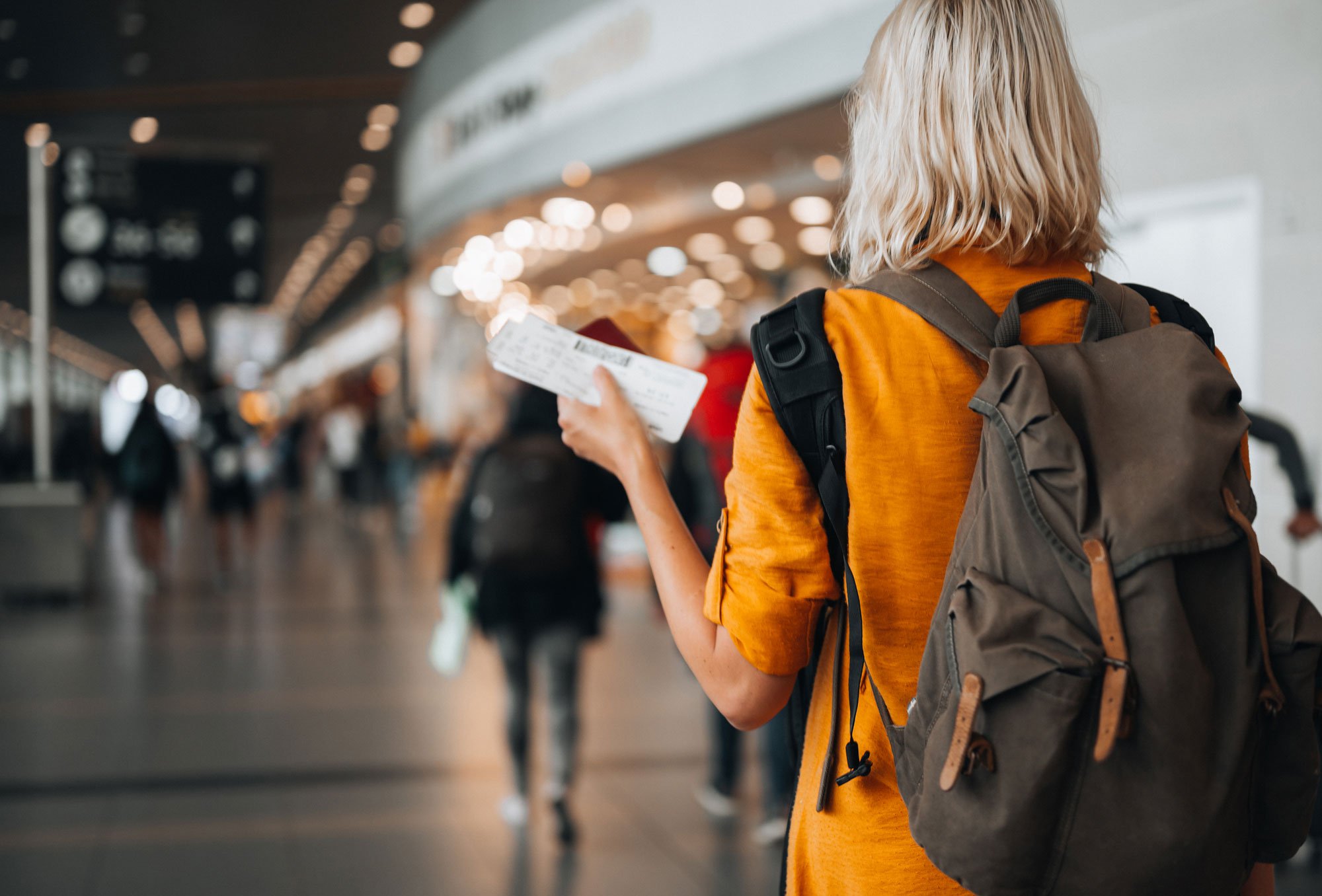 Woman walking through airport with backpack and holding ticket