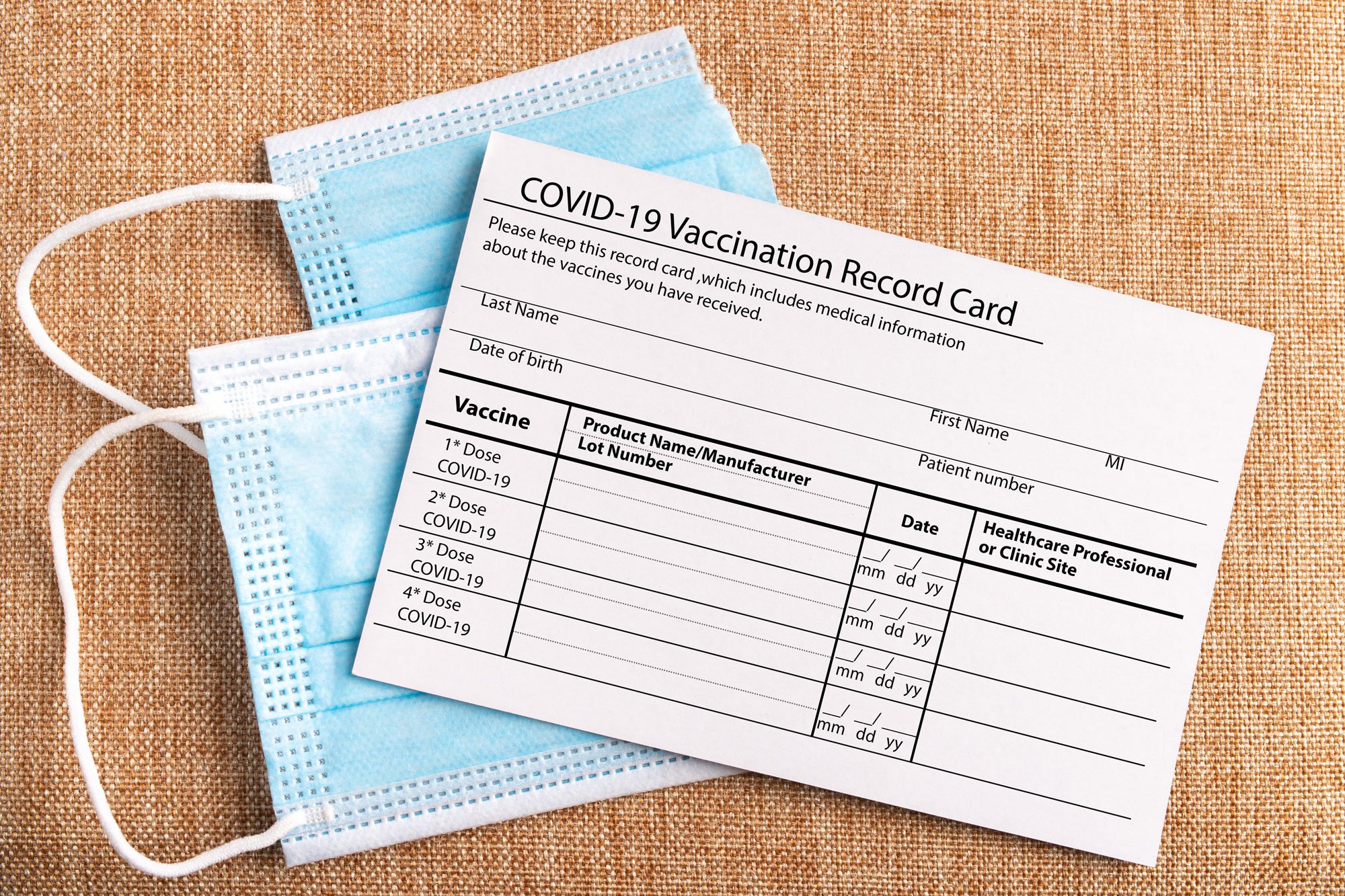 COVID-19 vaccination record card next to a medical procedure mask.