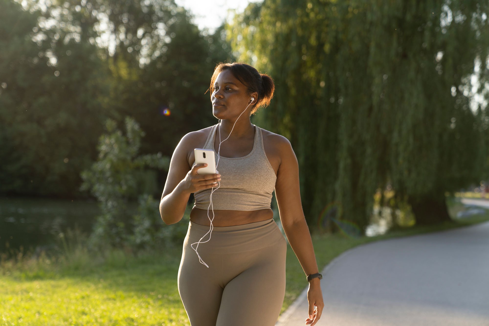 Young woman using phone and headphones while walking down a path